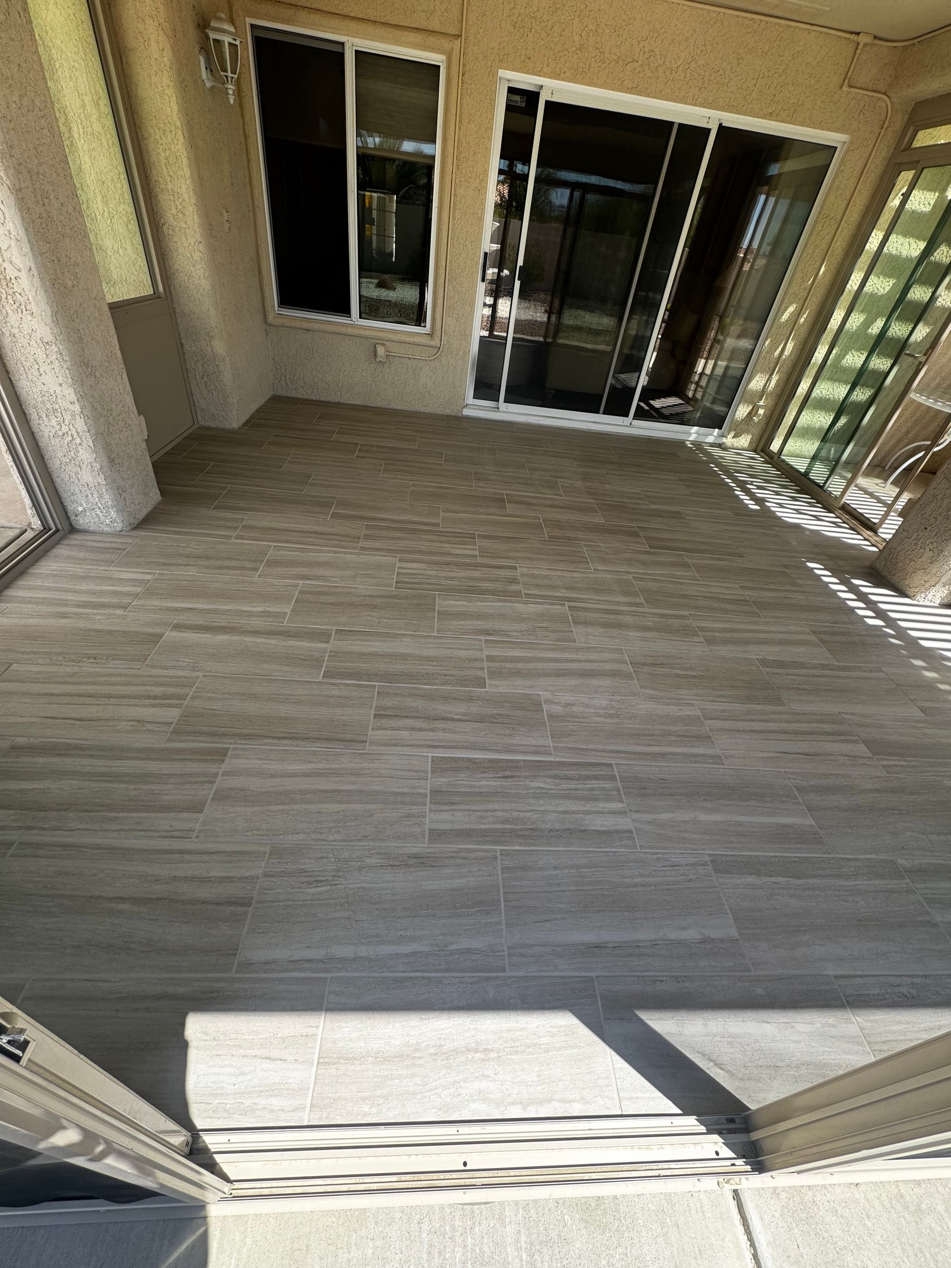 Tiled patio with sliding glass doors, concrete floor, and sunlight streaming in.