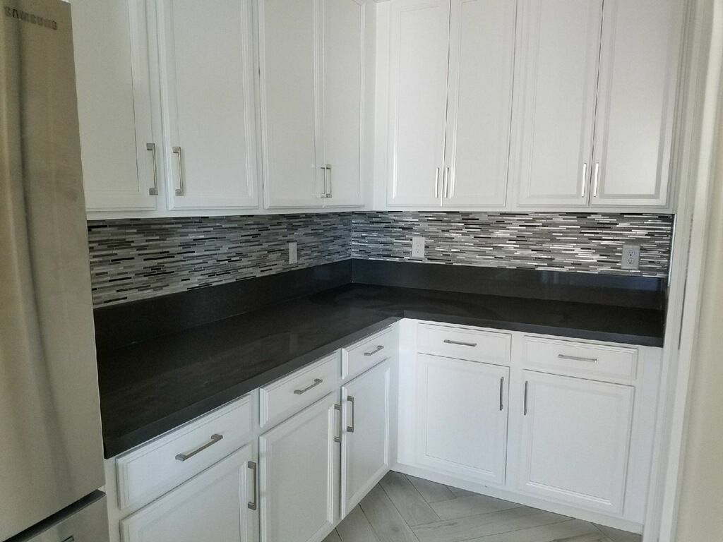 White cabinets, dark countertop in a kitchen, mosaic tile backsplash.