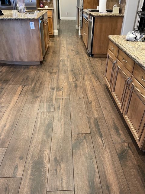 Wooden floor in a kitchen with light-colored cabinets, granite countertops, and stainless steel appliances.