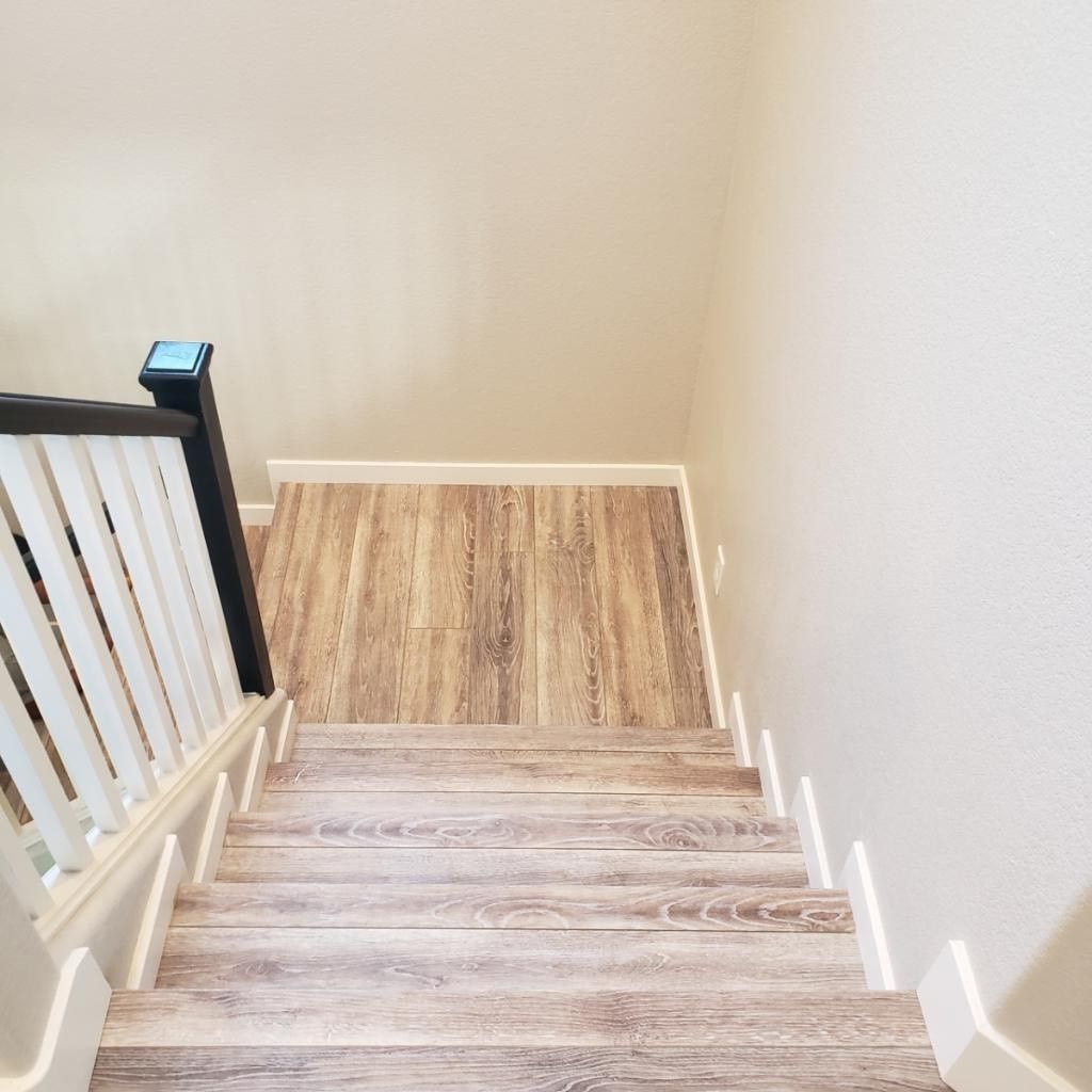 Wooden stairs leading down, white handrail on the left, beige walls.