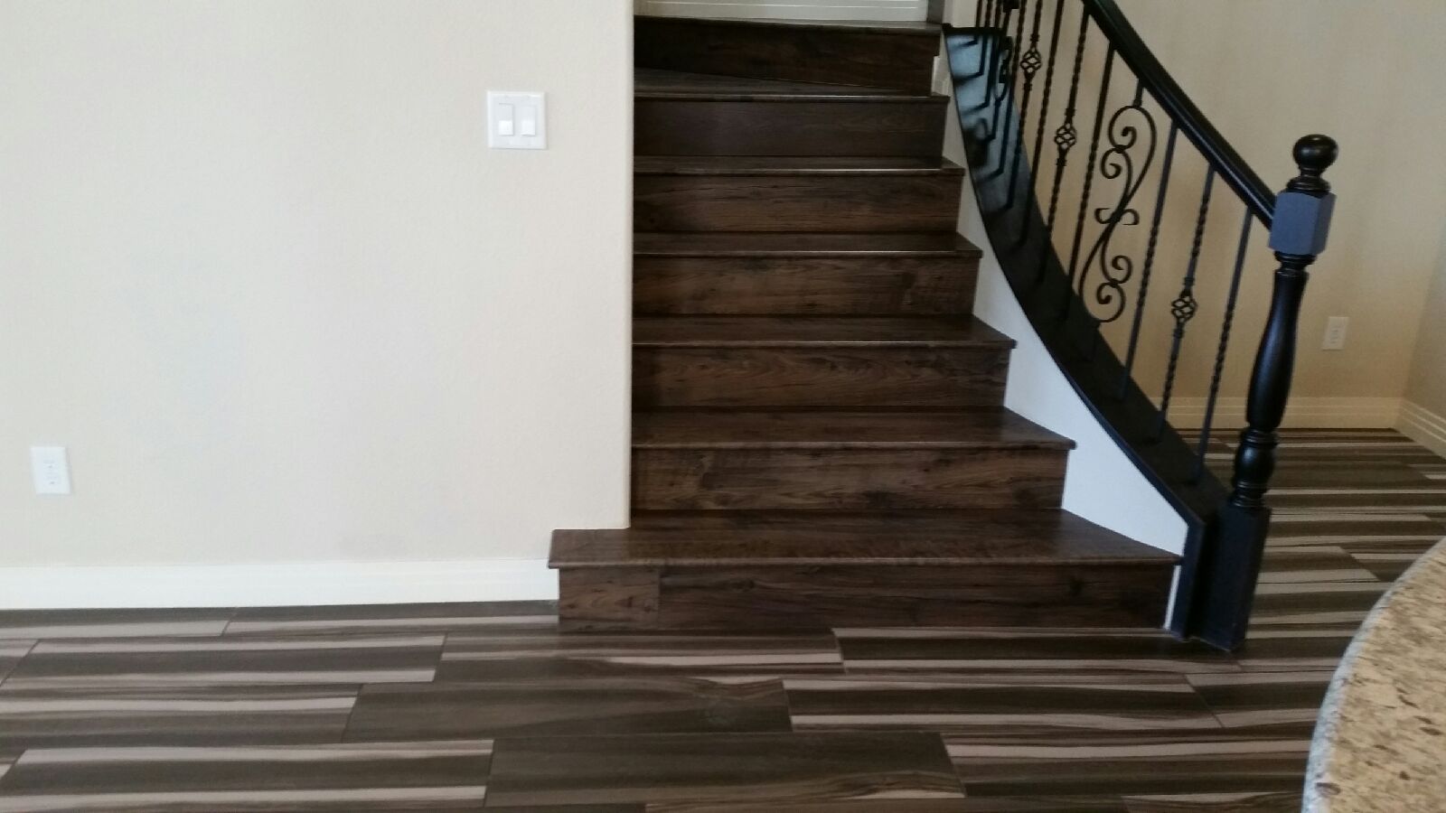 Dark wood staircase with black wrought iron railing, tan walls, and wood-look flooring.