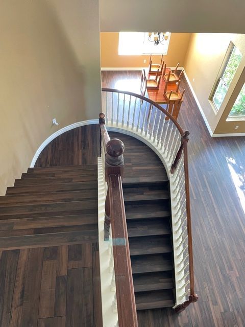 Overhead view of a curved staircase with dark wood treads, leading down to a dining area with chairs and a window.