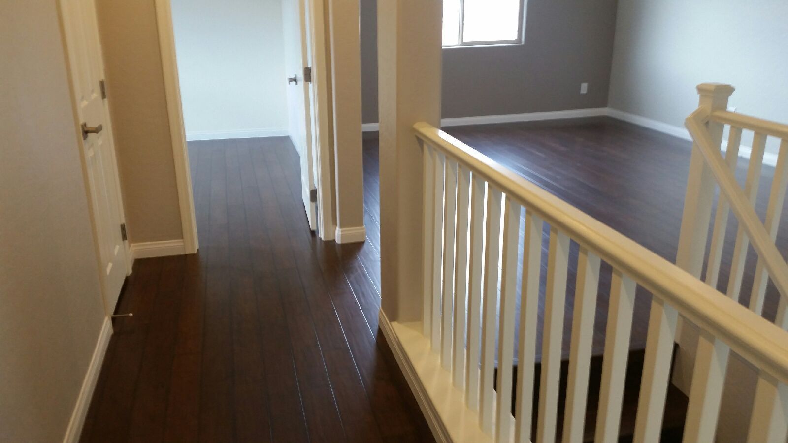 Hallway with dark wood floors, staircase, and doorway to a gray-walled bedroom.