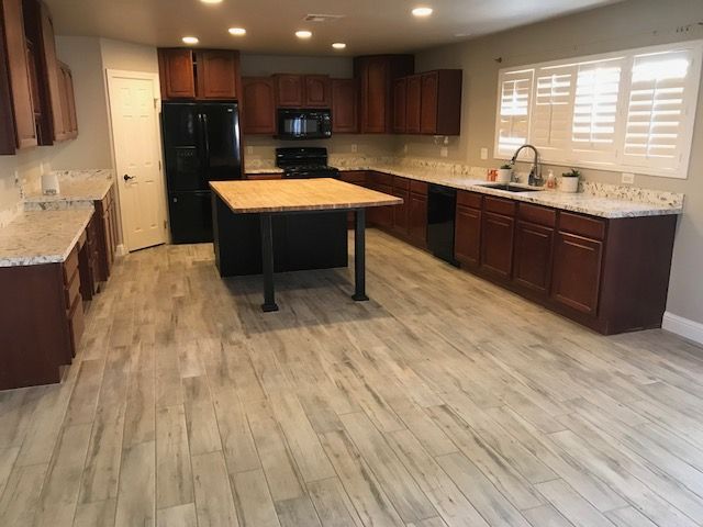 A large kitchen with wood cabinets, granite countertops, and wood-look flooring. An island sits in the center.