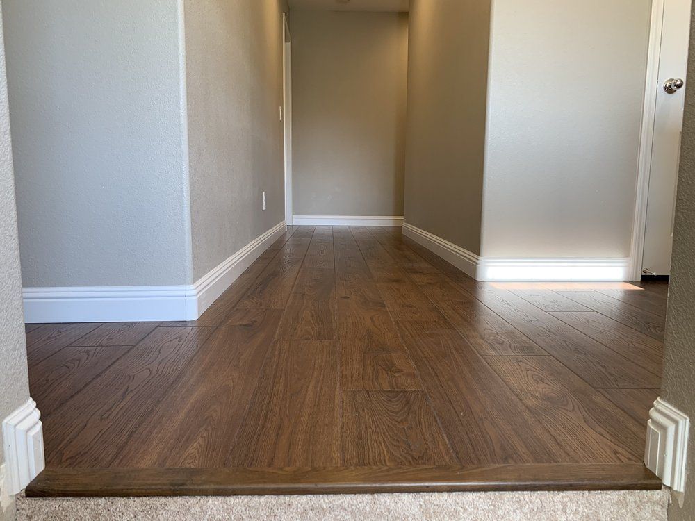 Hallway with wood floors, white trim, gray walls, and a doorway at the end.