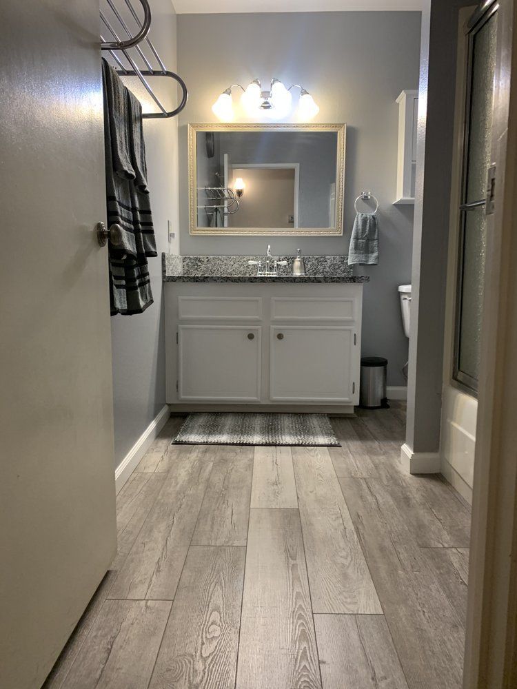 Bathroom with gray walls, wood-look floor, white vanity, mirror, towels, and a shower.