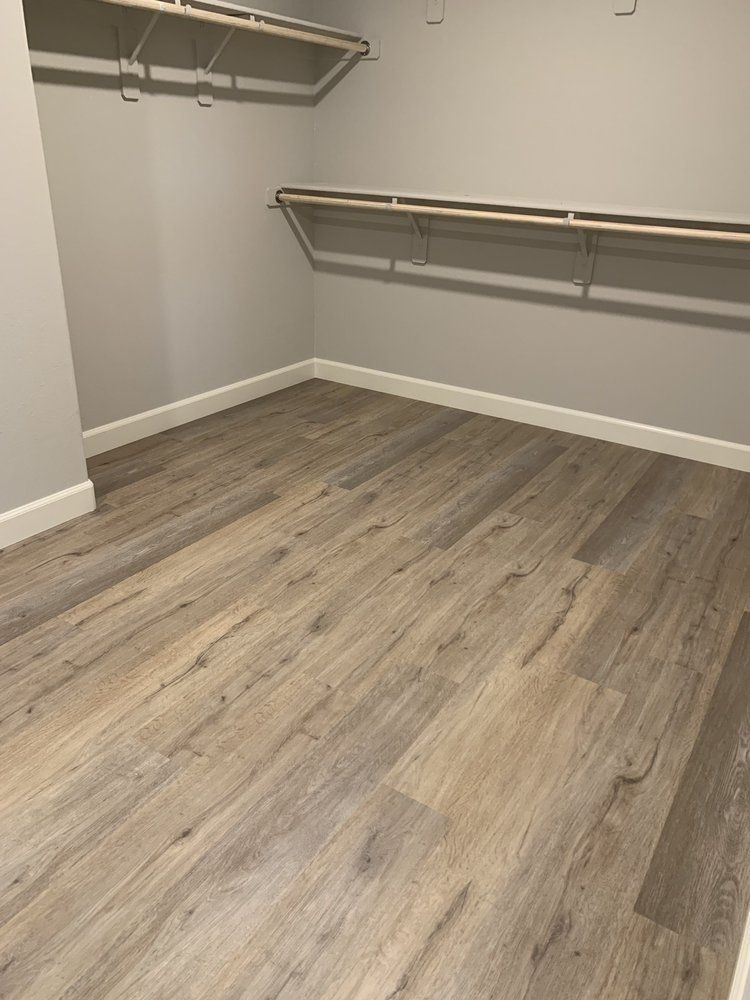 Empty walk-in closet with light wood-look flooring and gray walls, featuring shelves and a hanging rod.