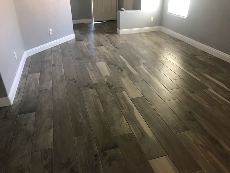 Wood-look tile floor in a room with gray walls and white baseboards; natural light shines in.