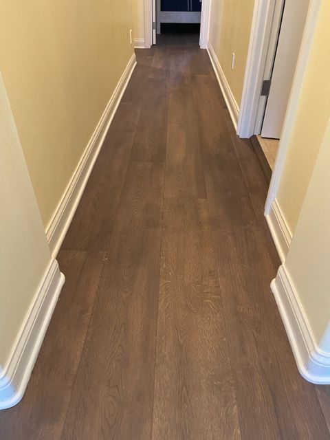 Hallway with brown wood floor, yellow walls, and white trim leading to a doorway.