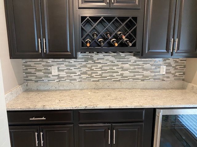 Kitchen cabinetry with a wine rack, light countertop, and a tiled backsplash.