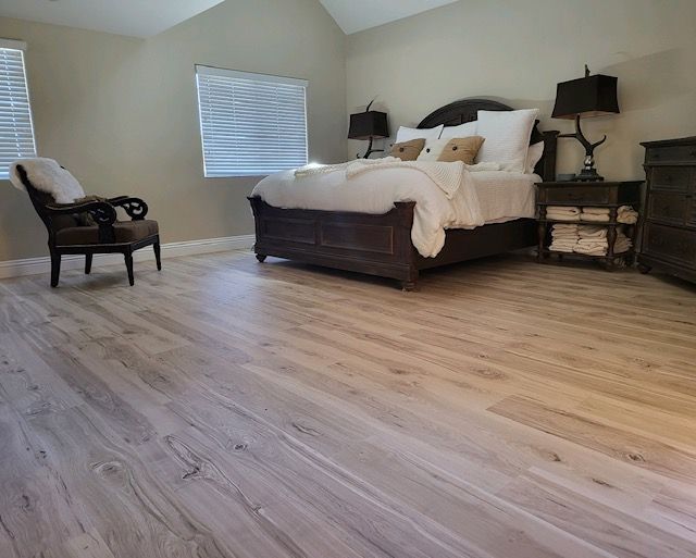 Bedroom with hardwood floors, king-size bed, bedside tables, chair, and windows.