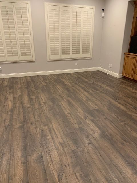 Empty room with wood-look flooring, white shutters, gray walls, and wooden cabinets.