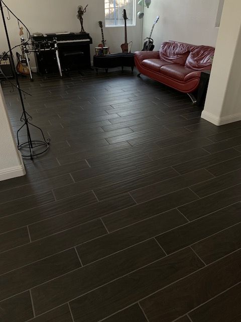 Dark wood-look tile floor in a living space, with a red couch and guitars visible.