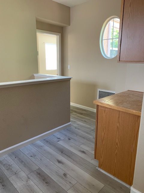 Interior view of a hallway with hardwood floors, a wall, cabinet, and an oval window.