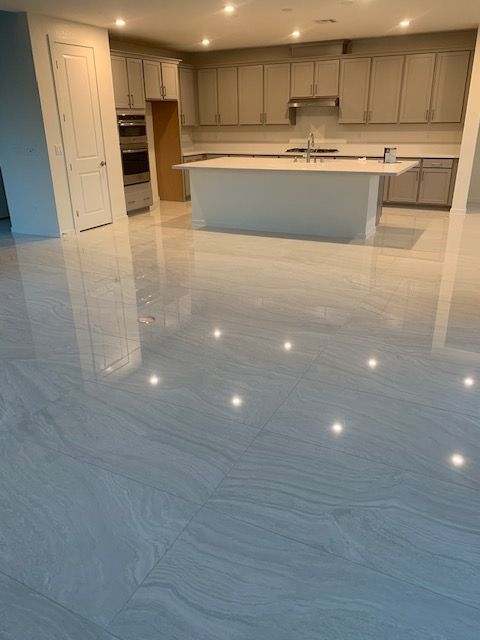 Bright kitchen with light gray cabinets, white island, and glossy, patterned marble-like flooring.