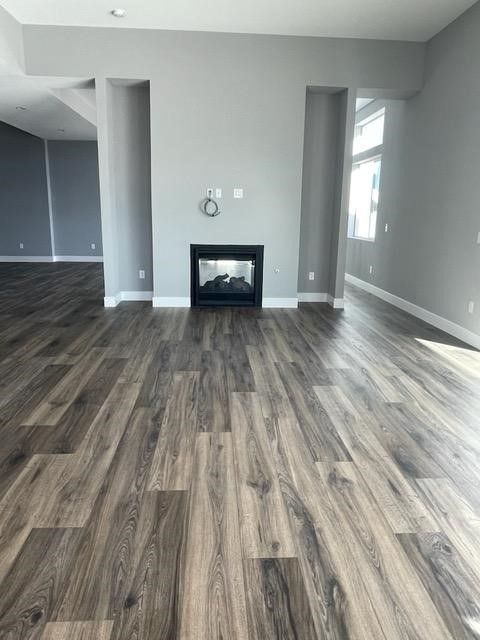 Empty living room with dark wood-look flooring, gray walls, fireplace, and recessed side areas.