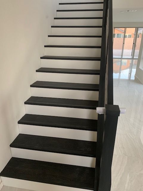 Staircase with dark treads and white risers; dark railing on the right, white wall on the left.