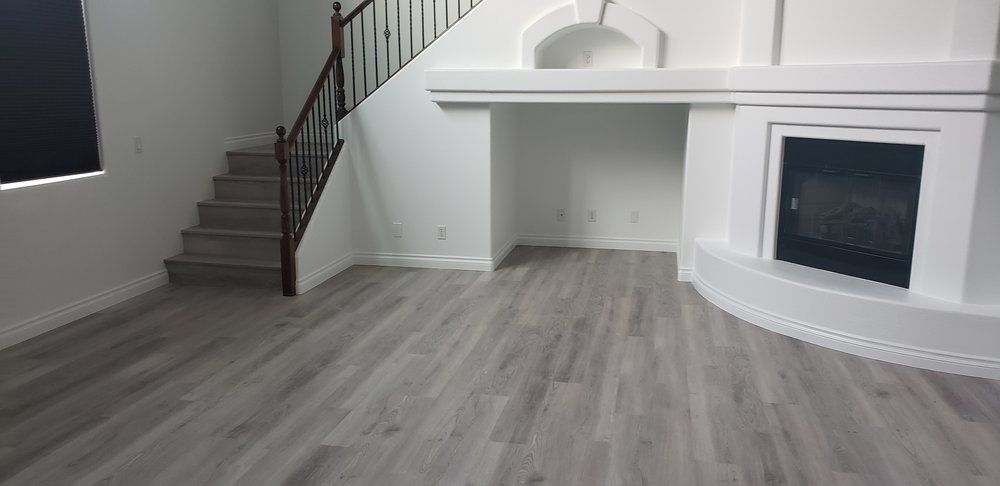 Empty living room with gray wood floors, a staircase, and a white fireplace.
