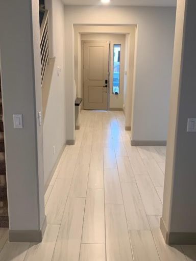 Hallway with white tile floor leading to a beige front door with sidelight. Staircase on the left.
