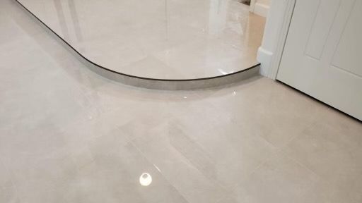Light beige tiled floor with curved metal transition strip, leading to white door frame.