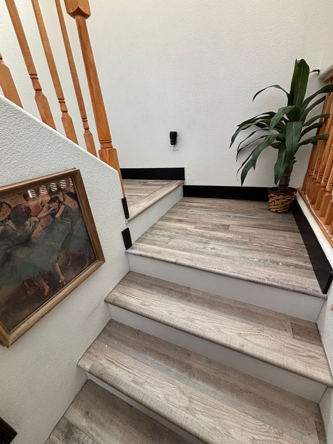 Staircase with wood-look treads, a framed picture, and a potted plant, leading upward.