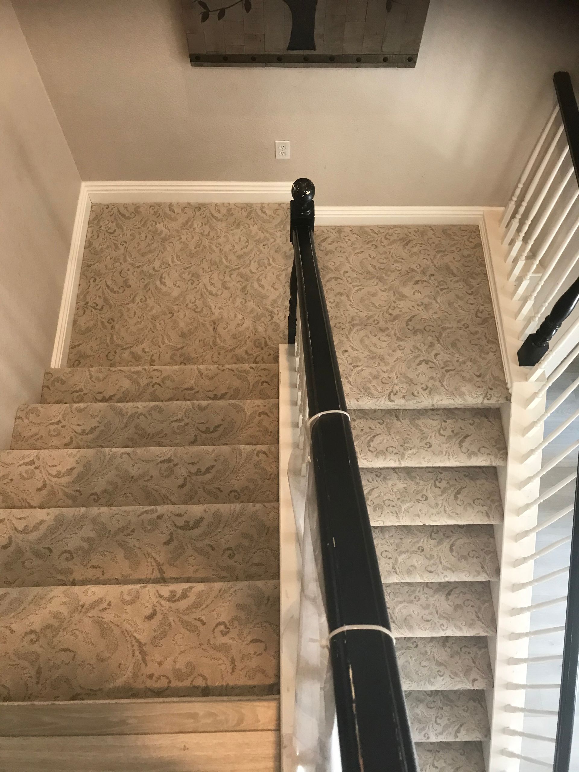 Staircase with beige carpet and black handrail descending from a hallway.