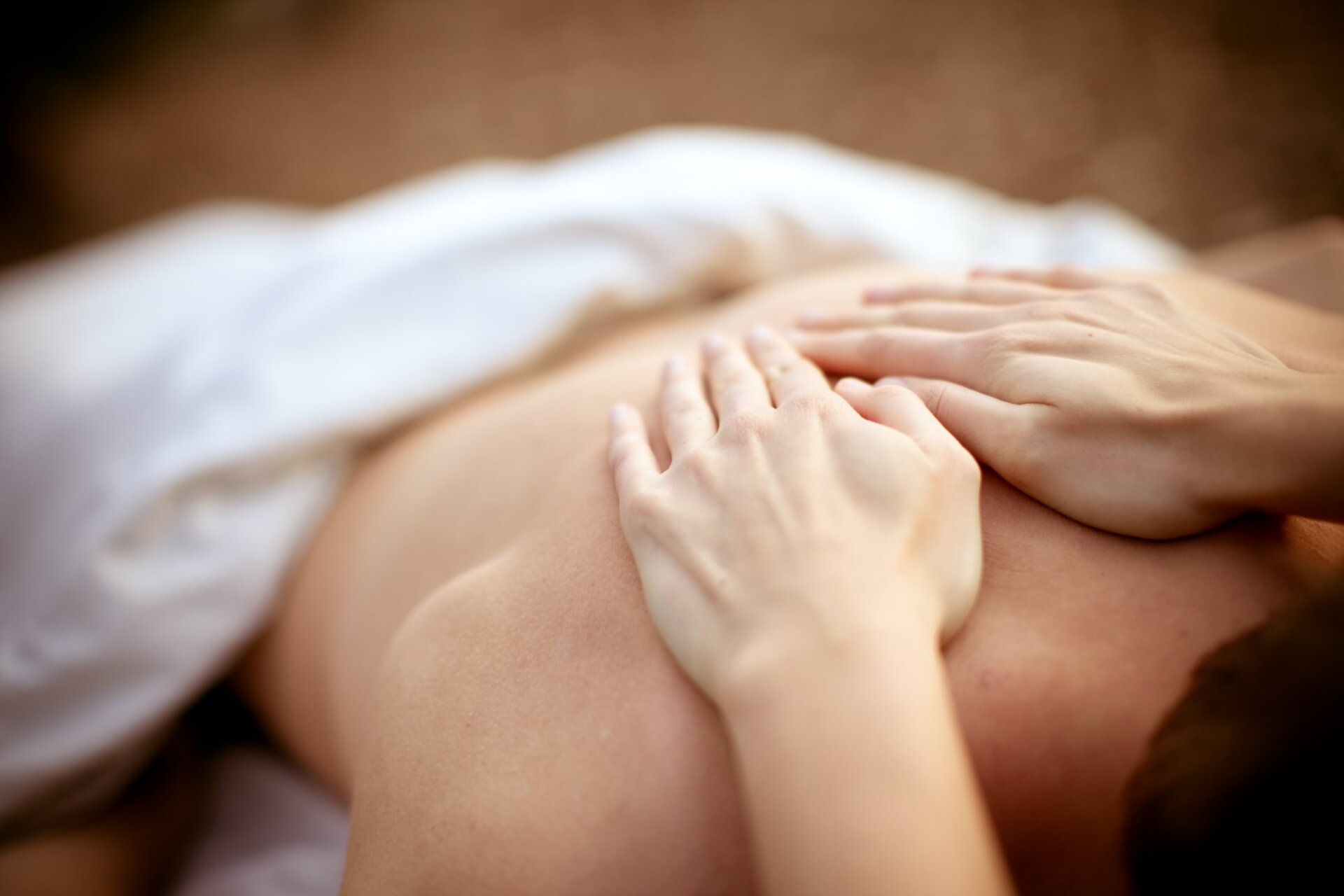 Hands massaging a person's bare back, partially covered by white sheet.
