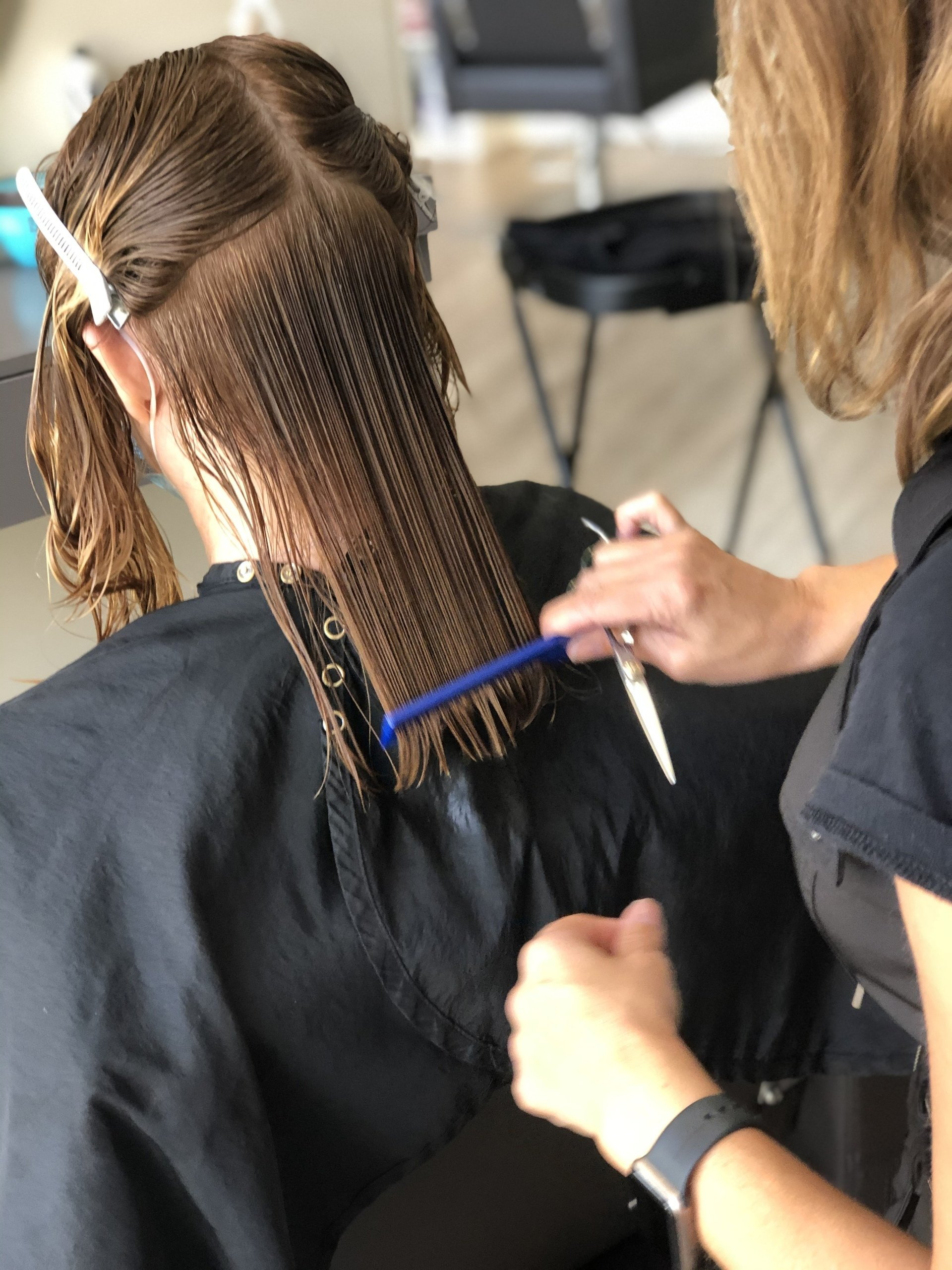 Hair stylist cutting a client's wet hair with comb and scissors in a salon setting.