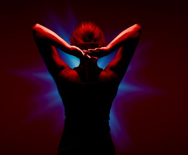 Woman with hands behind her head, back to viewer, red and blue lighting.