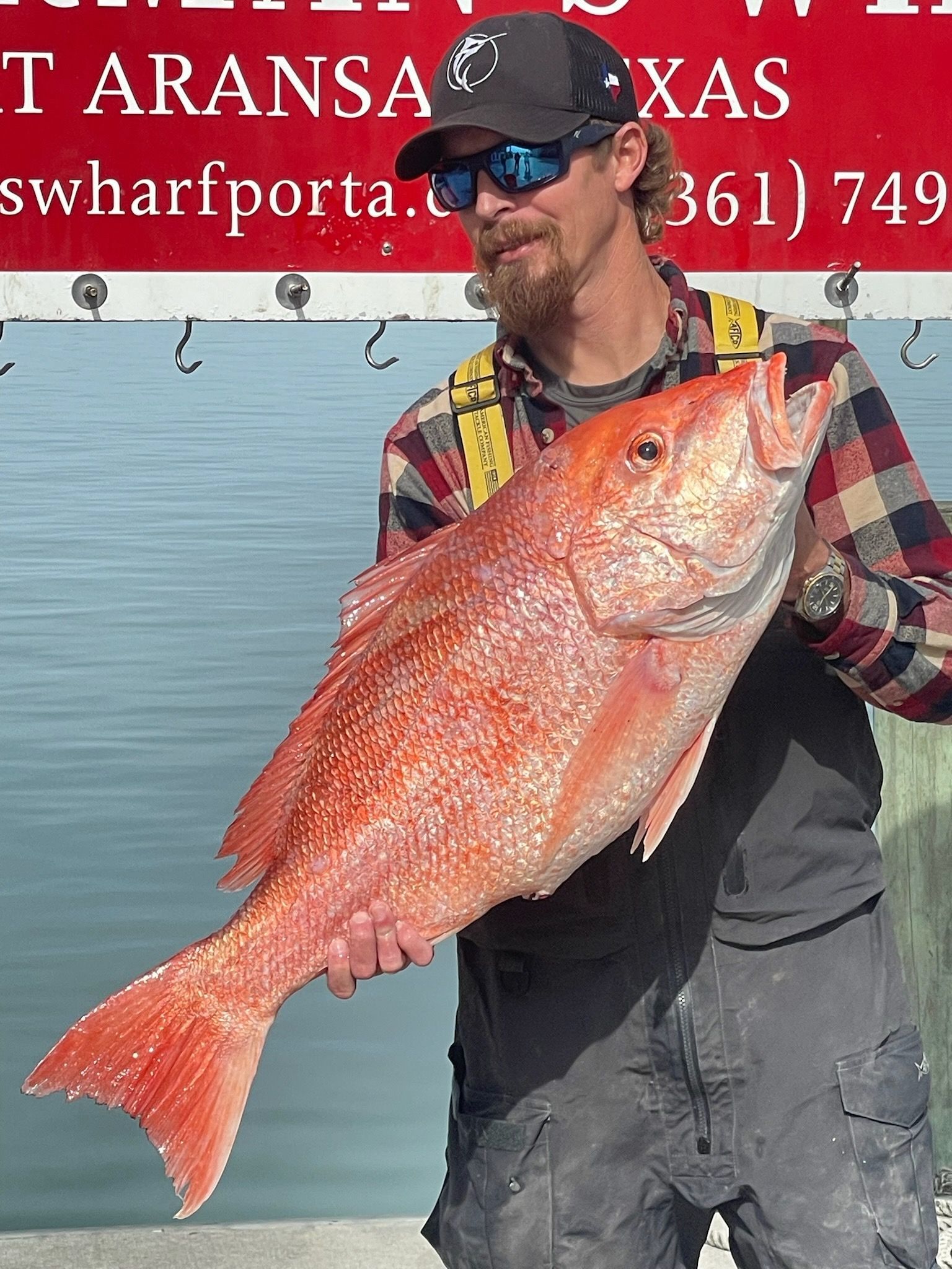 A man is holding a large red fish in front of a sign that says swharfporta
