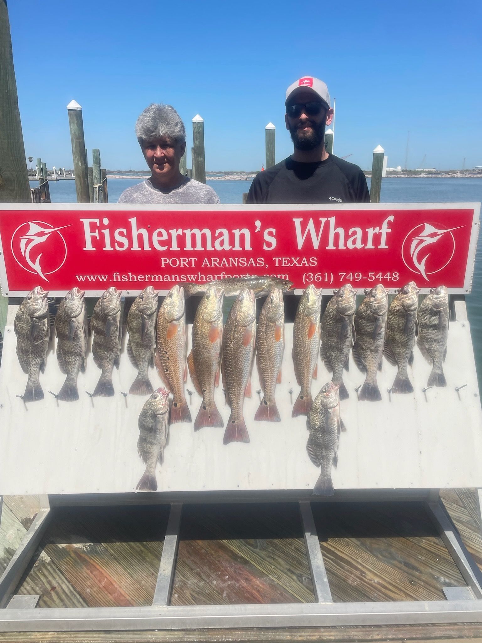 Two men are standing next to a sign that says fisherman 's wharf.