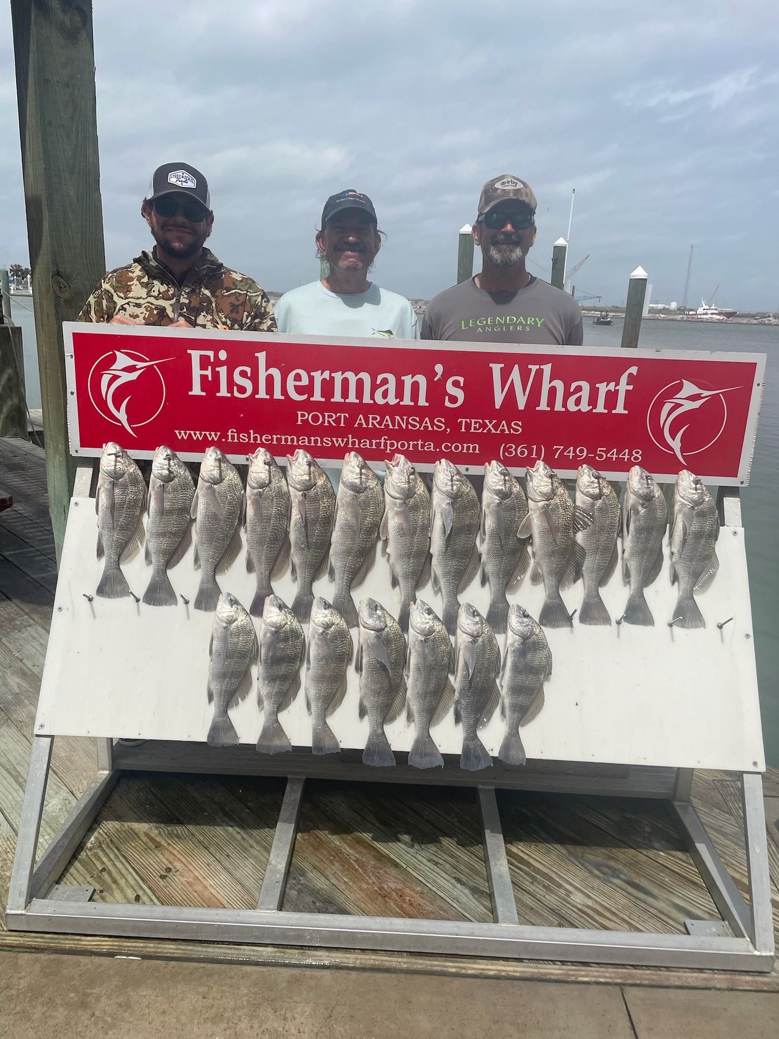 Three men are standing in front of a sign that says fisherman 's wharf.