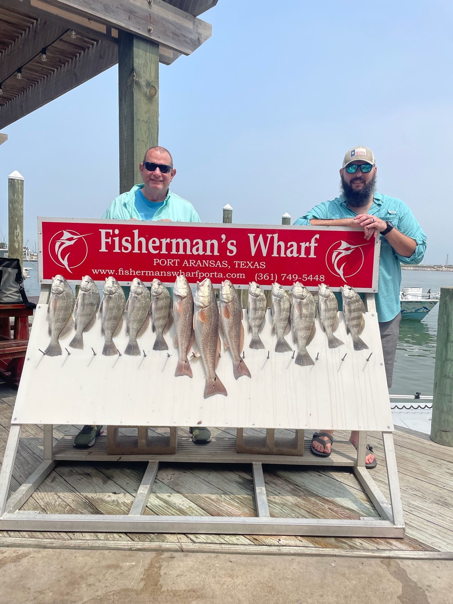 Two men are standing next to a sign that says fisherman 's wharf.