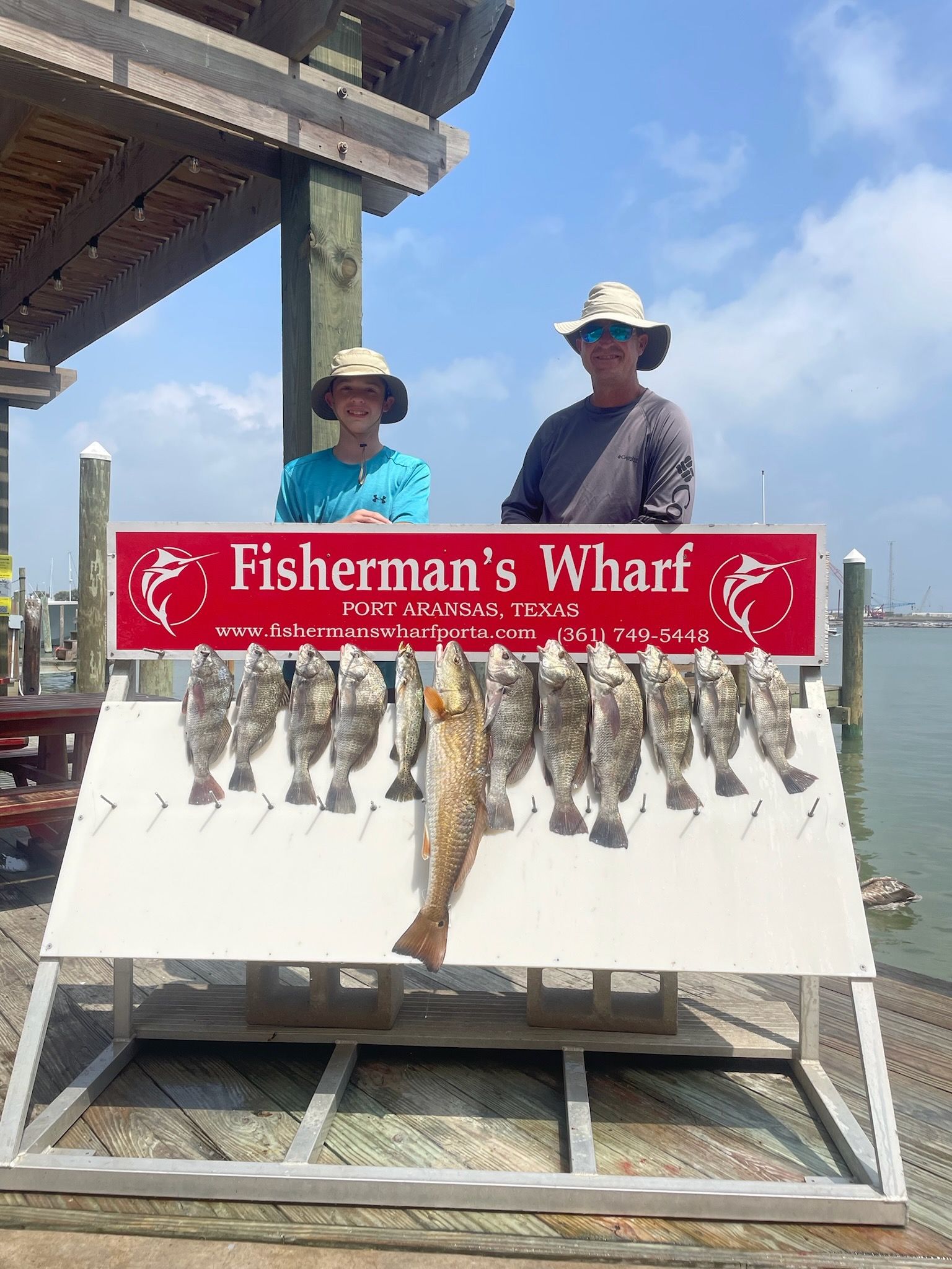 Two men are standing next to a sign that says fisherman 's wharf.