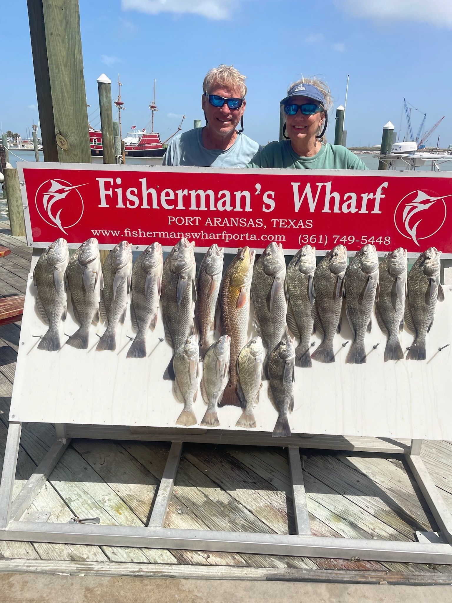 A man and a woman are standing next to a sign that says fisherman 's wharf.