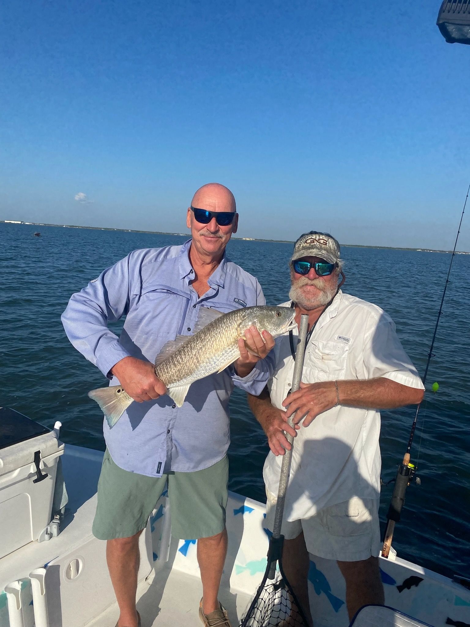 Two men are standing on a boat holding a fish.