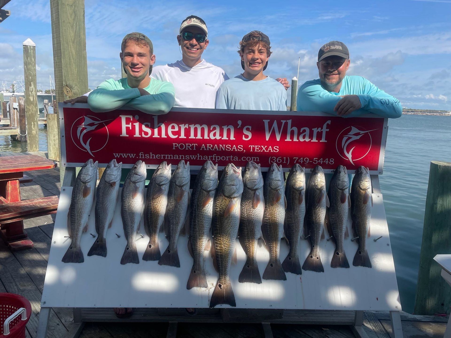 A group of men are standing next to a sign holding a bunch of fish.