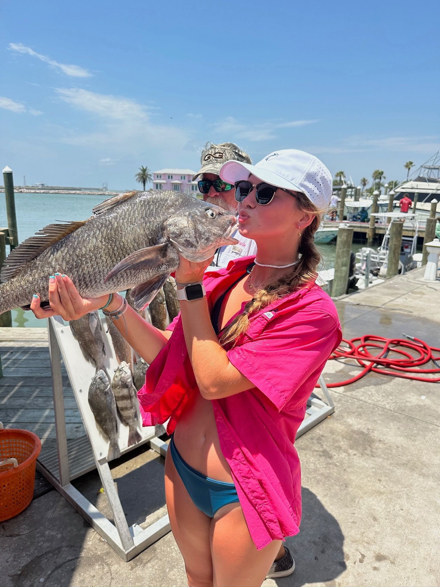 A woman in a bikini is holding a large fish in her hands.