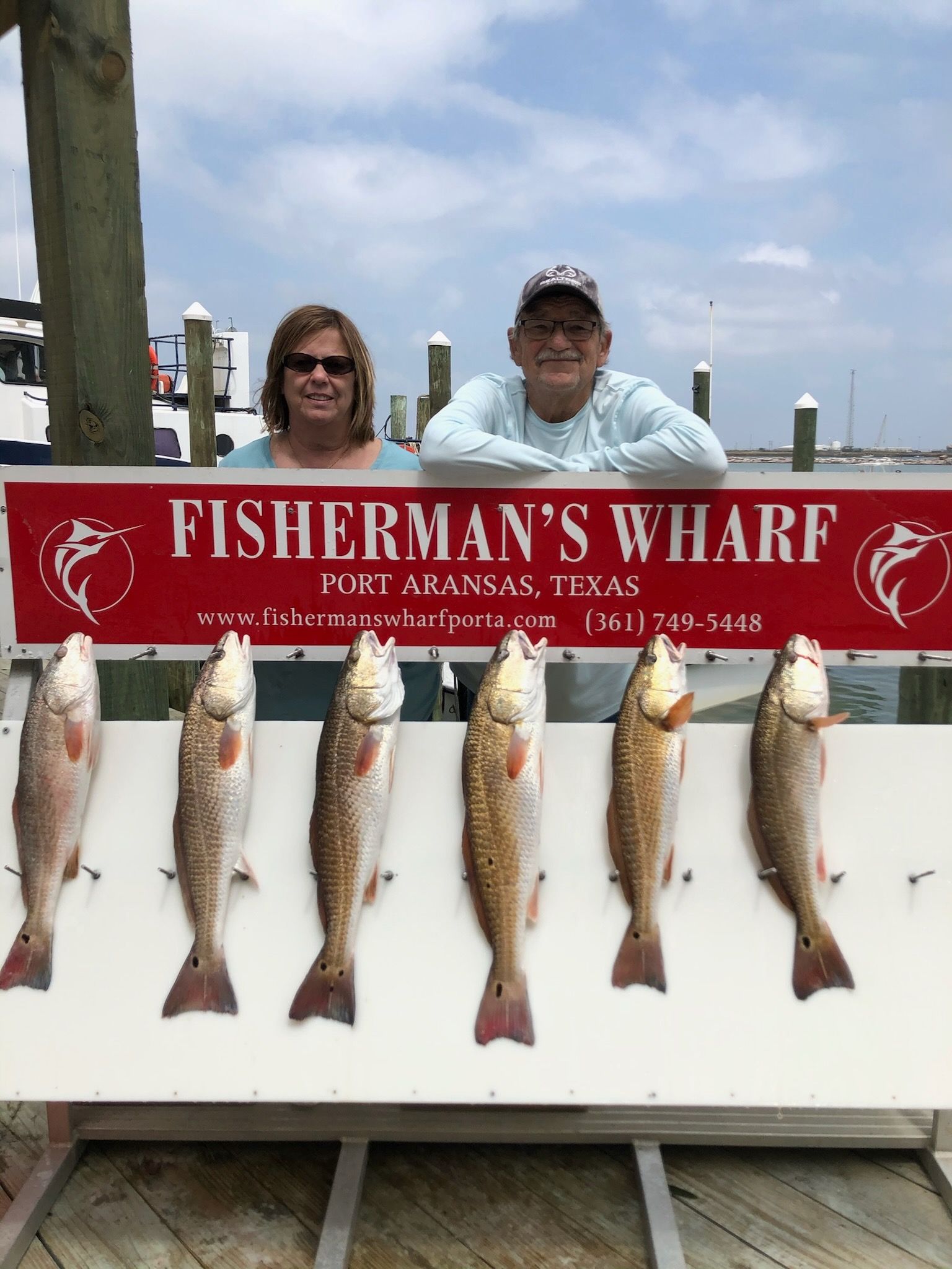 A man and woman are standing next to a sign that says fisherman 's wharf