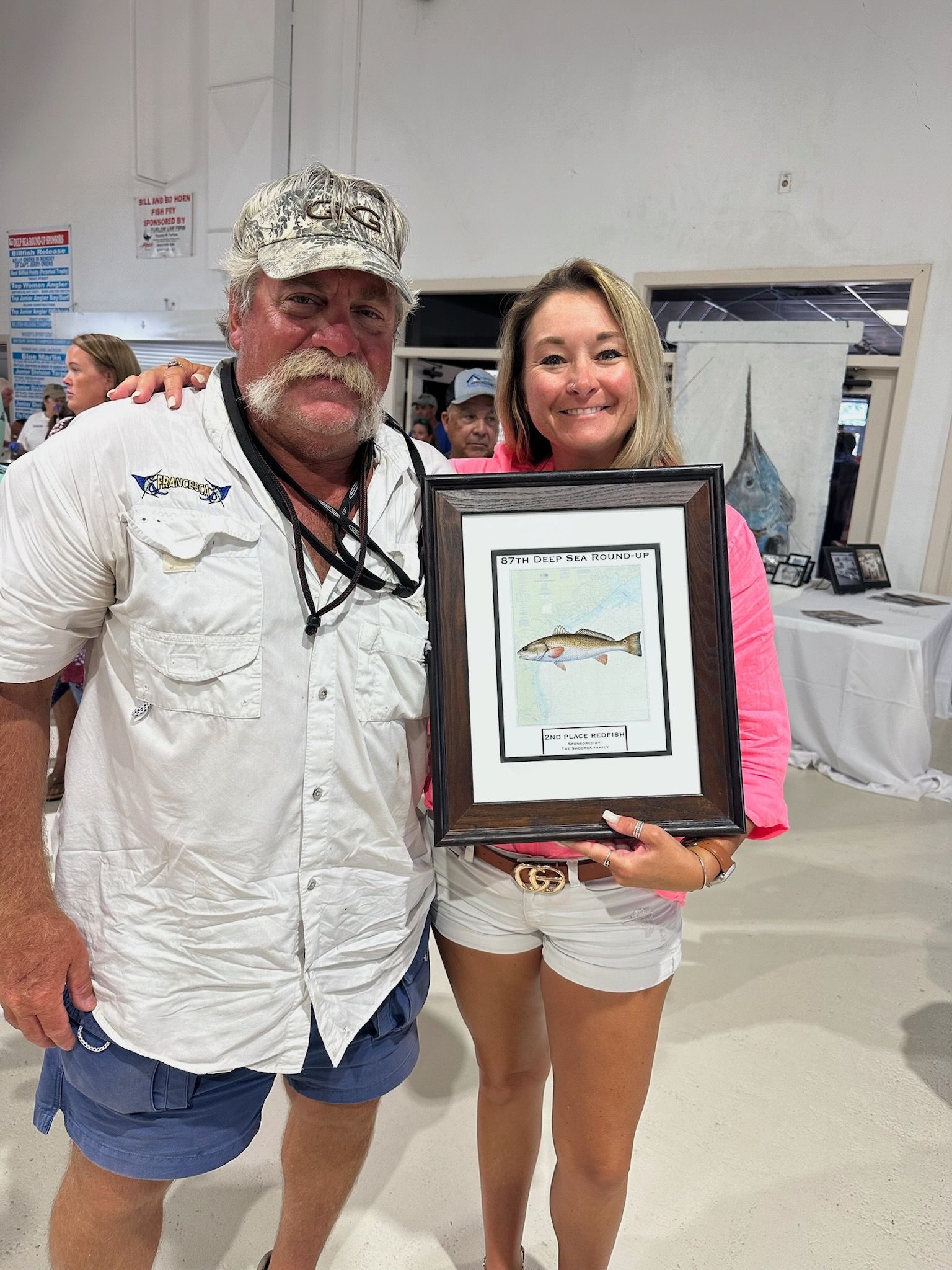A man and a woman are standing next to each other holding a framed picture of a fish.