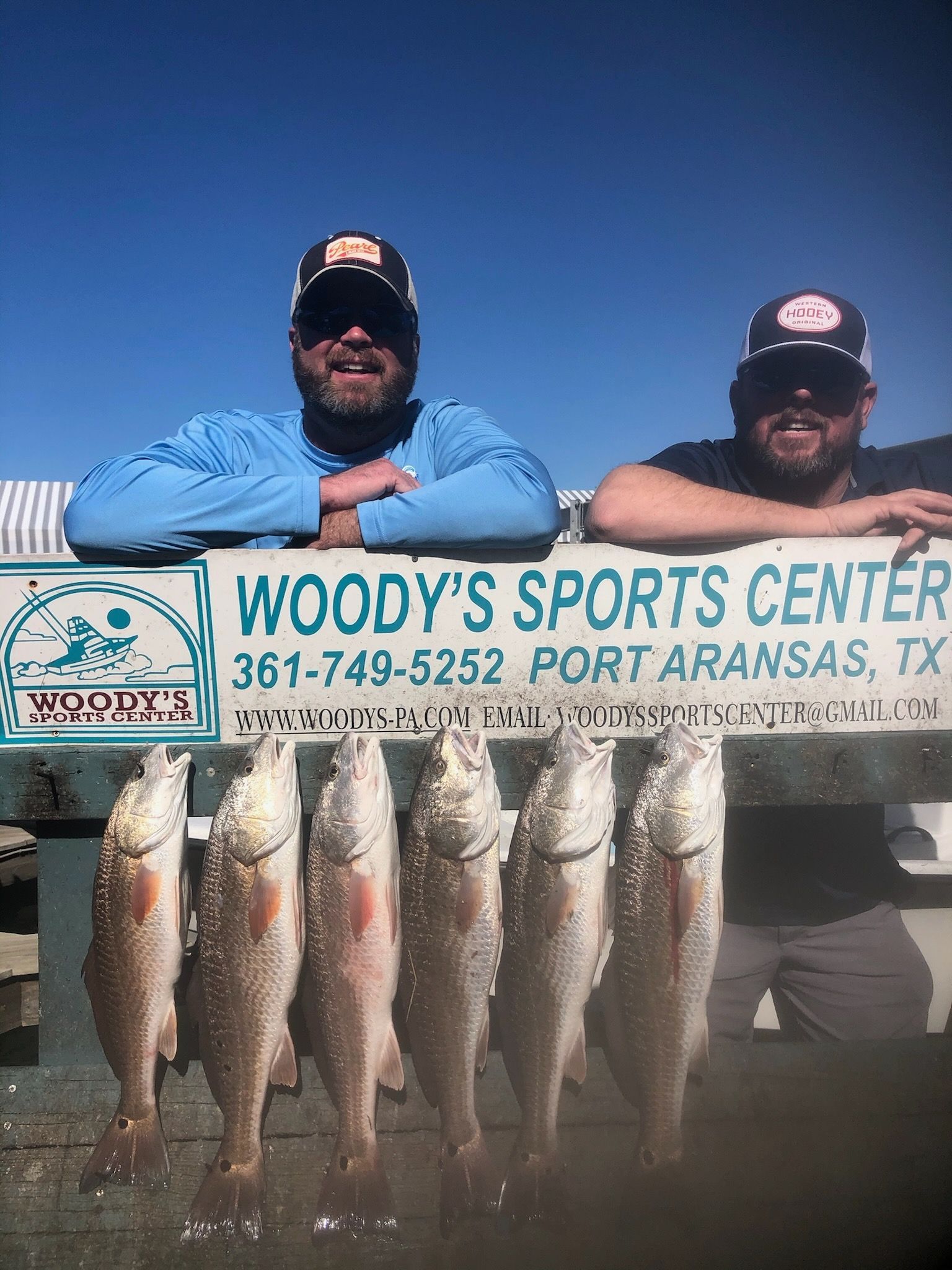 Two men are standing next to each other holding a bunch of fish.
