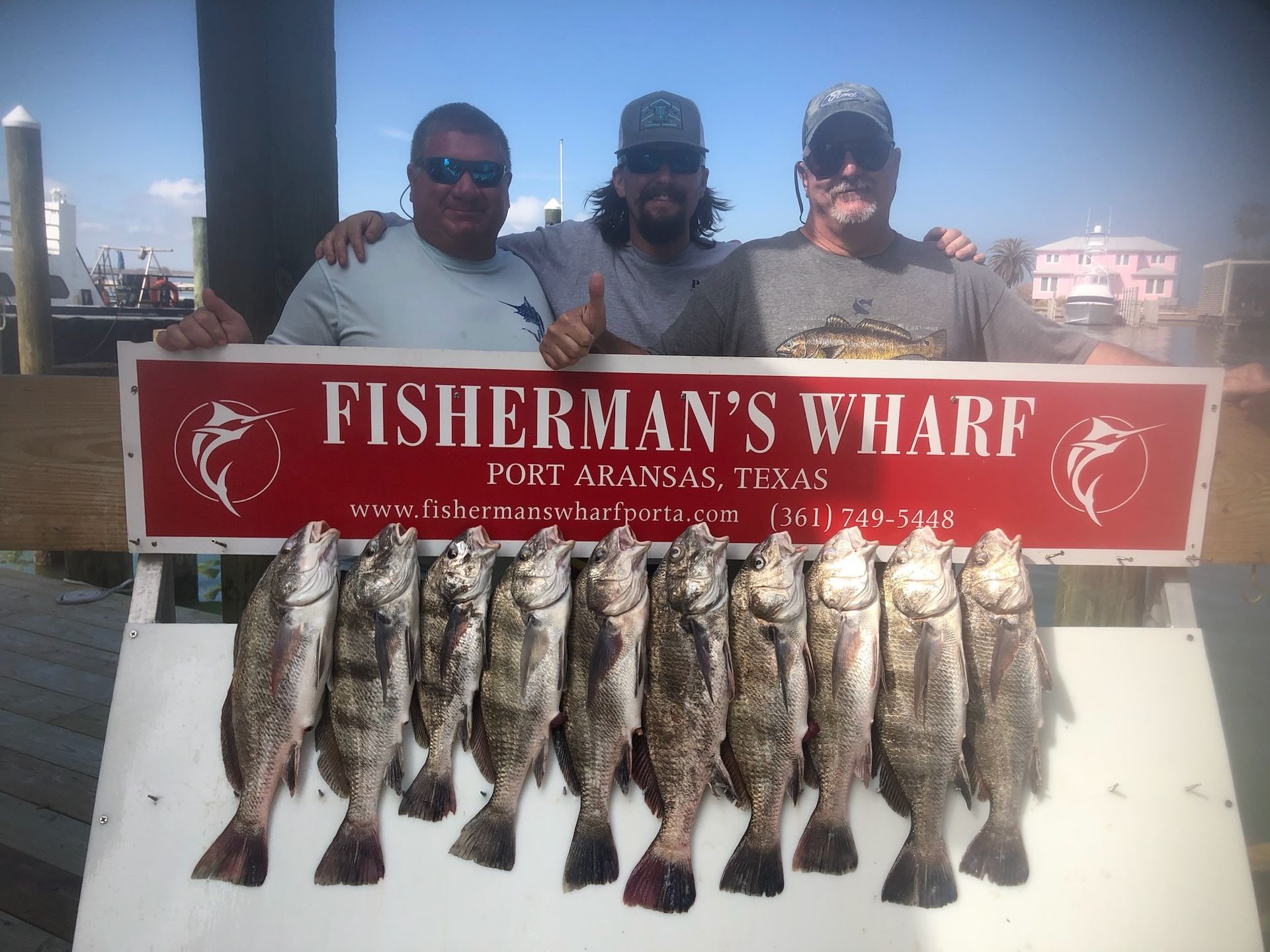 Three men are standing next to a sign that says fisherman 's wharf.