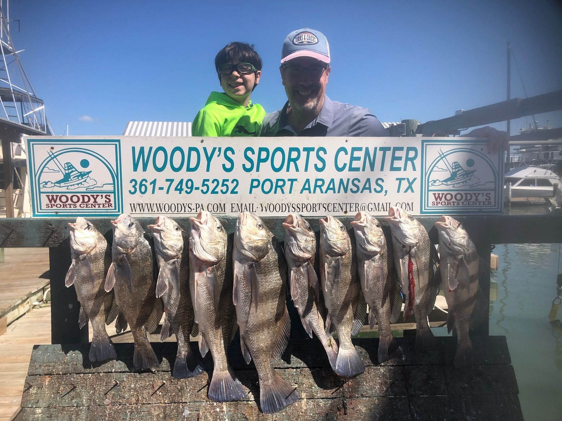 A man and a boy are holding a bunch of fish in front of a woody 's sports center sign.