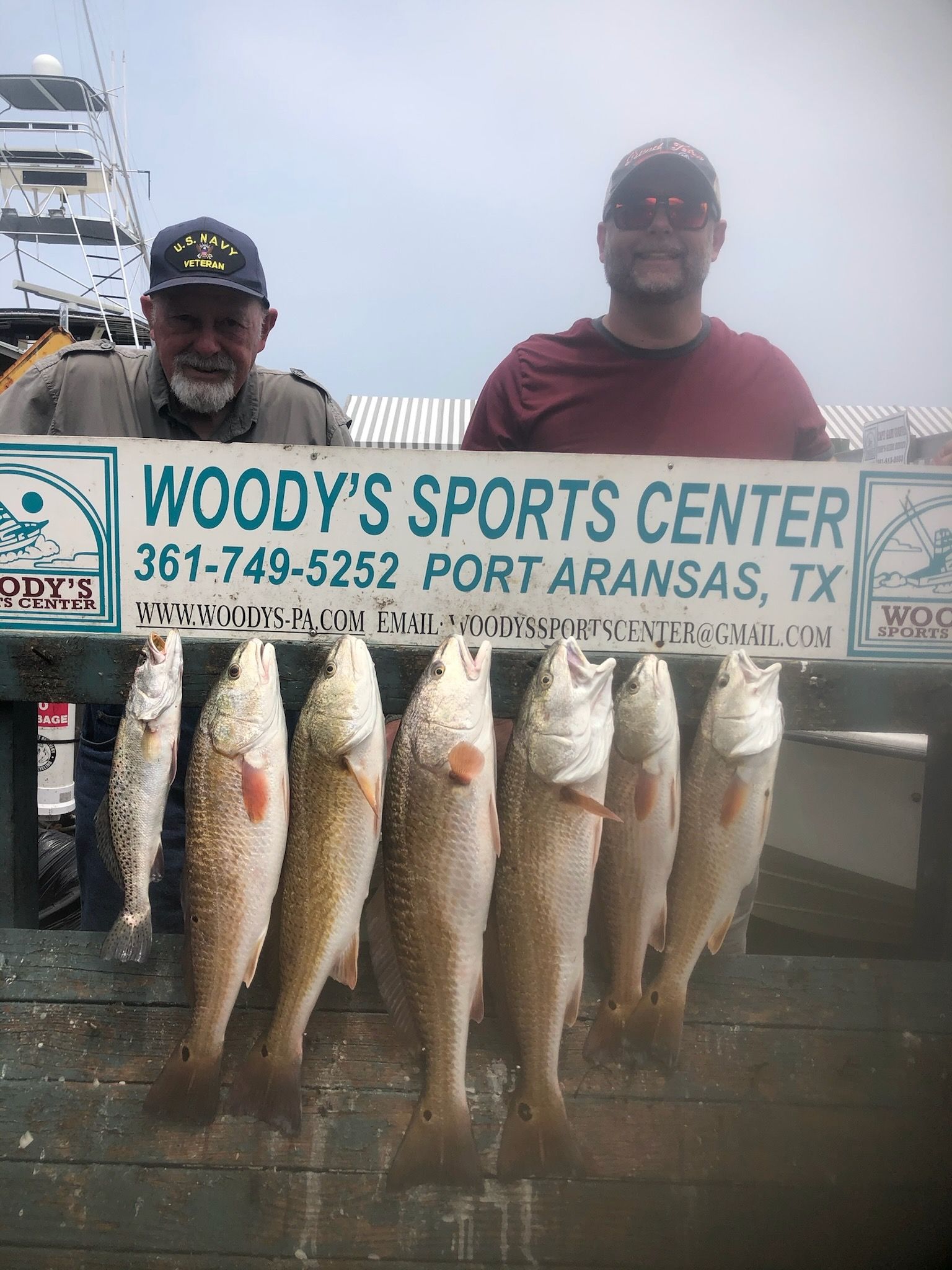 Two men are holding a sign that says woody 's sports center.