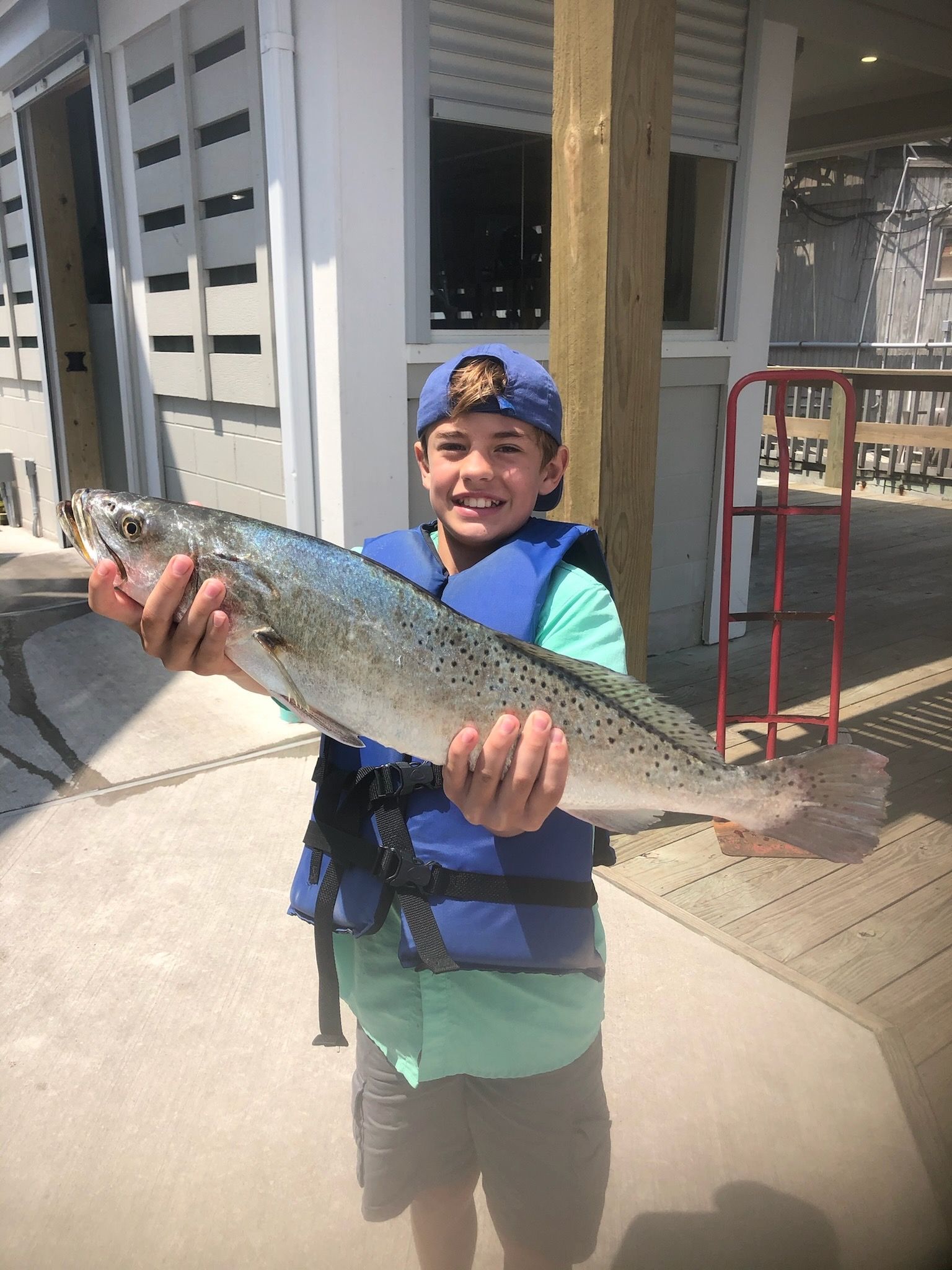 A young boy is holding a large fish in his hands.