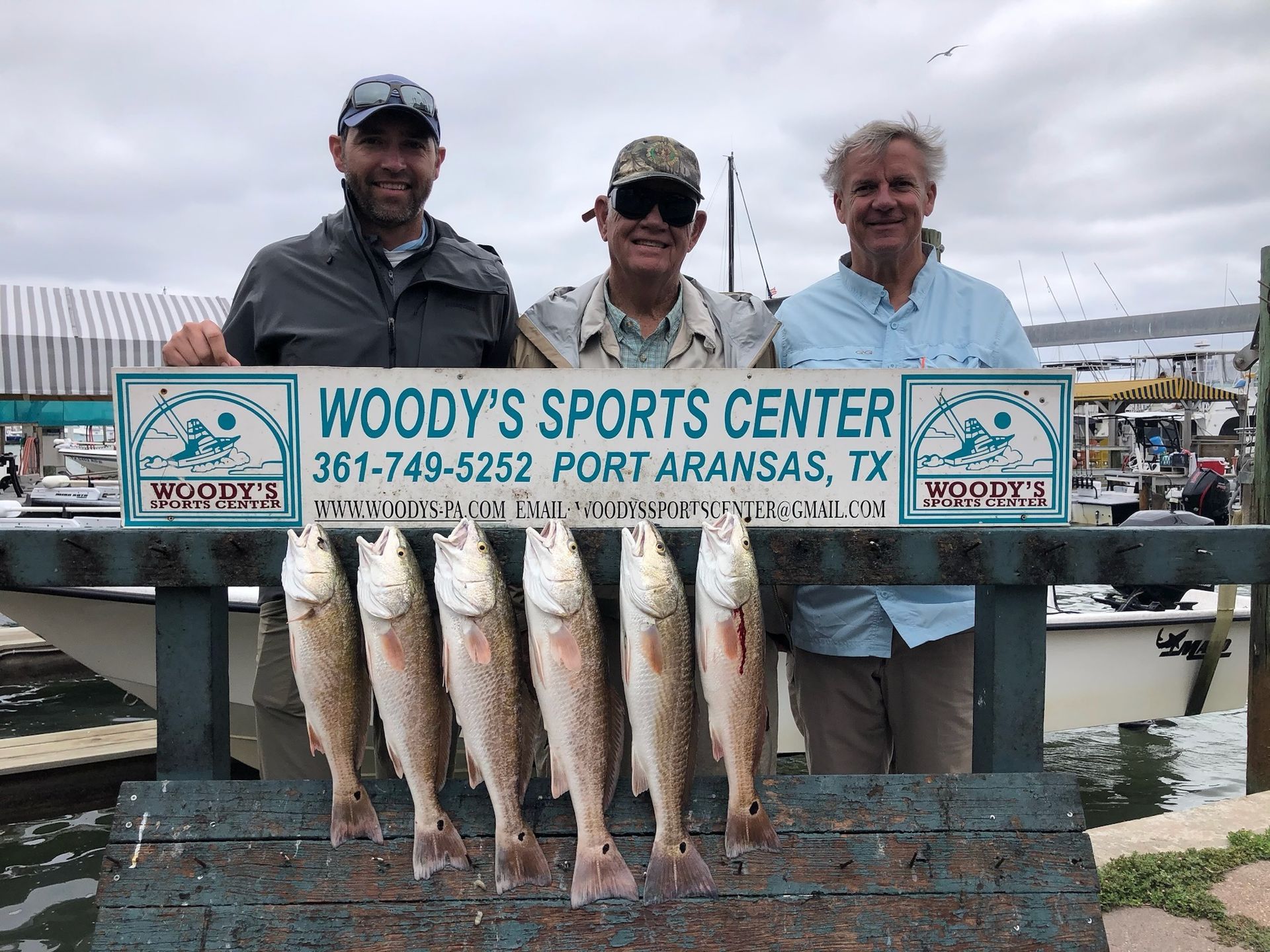 Three men are standing next to each other holding a sign that says woody 's sports center.