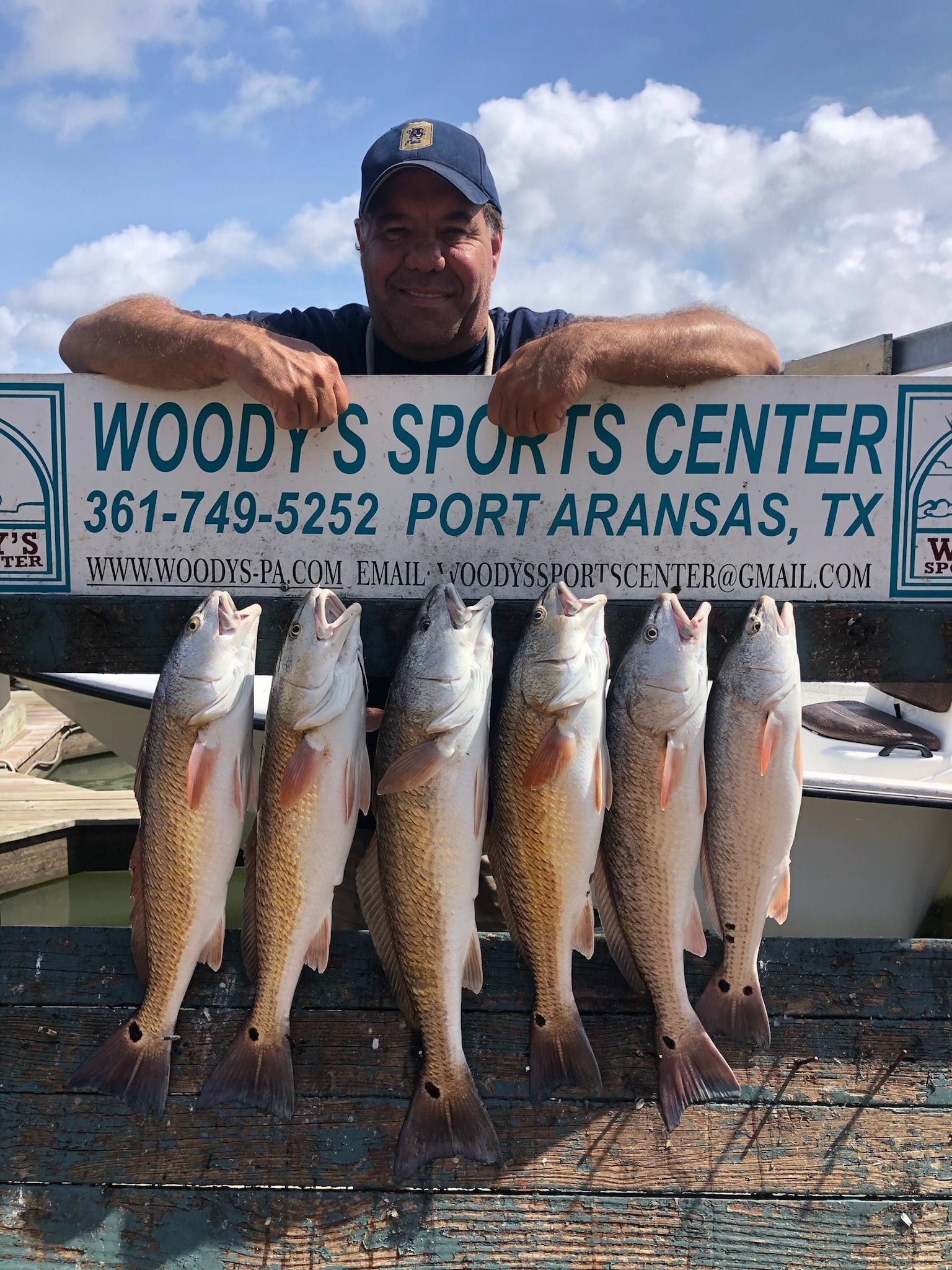 A man is holding a bunch of fish in front of a woody 's sports center sign.
