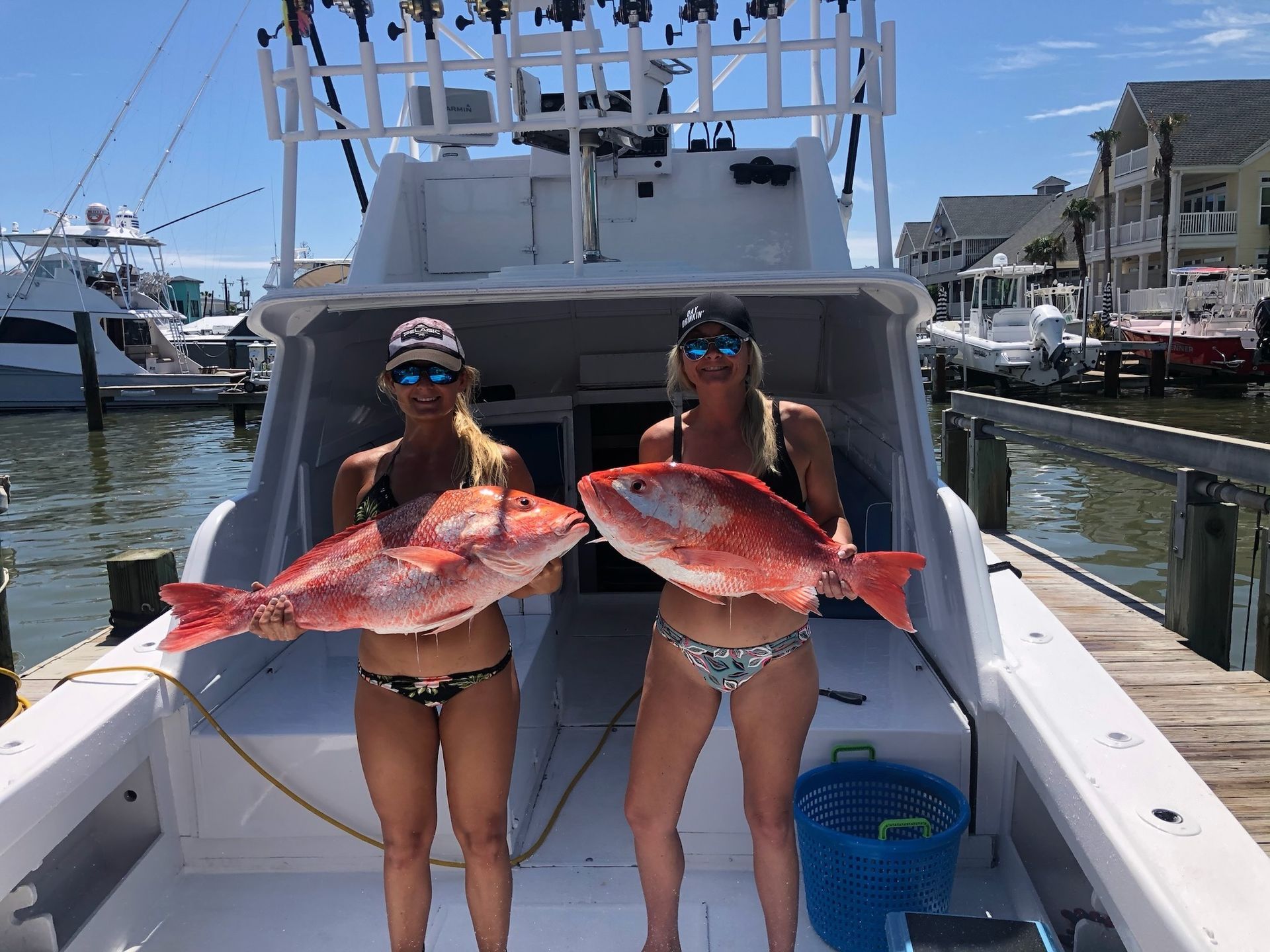 Two women in bikinis are holding large fish on a boat