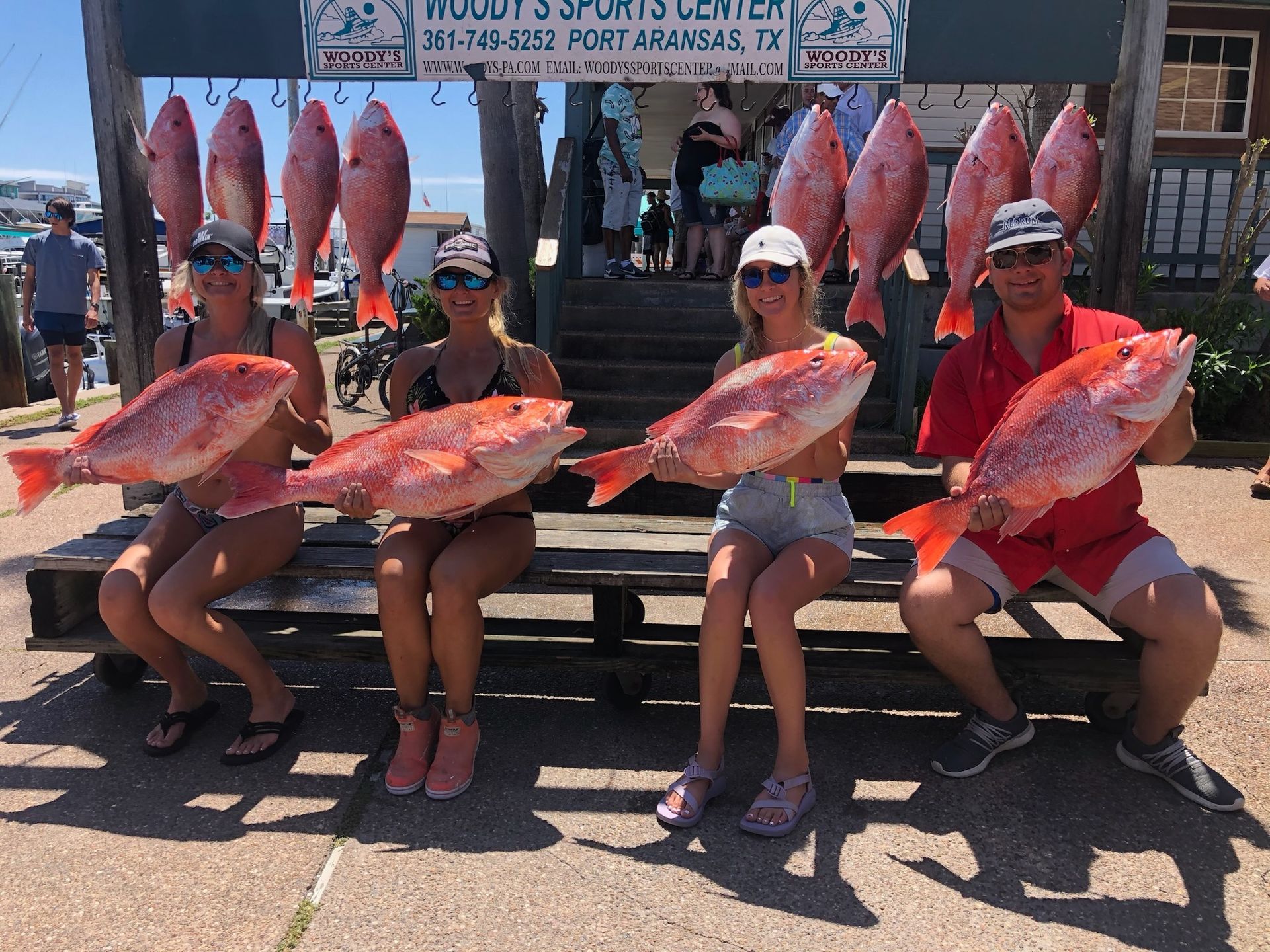 A group of people sitting on a bench holding large fish
