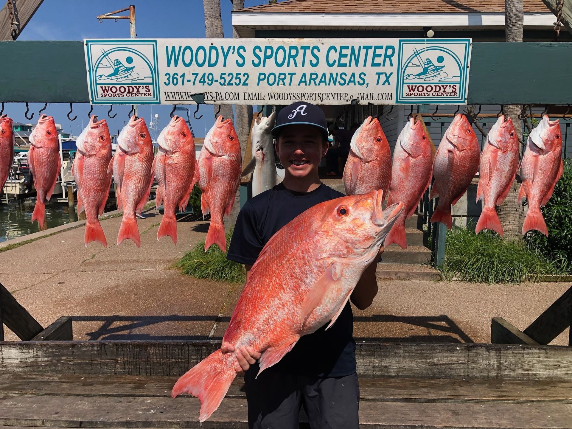 A man is holding a large red fish in front of a woody 's sports center sign